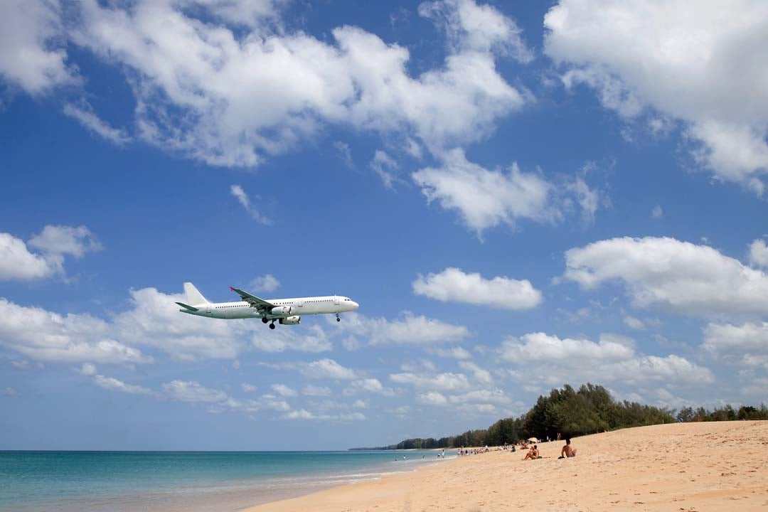 Plane lands over the beach with people on a Sunny day