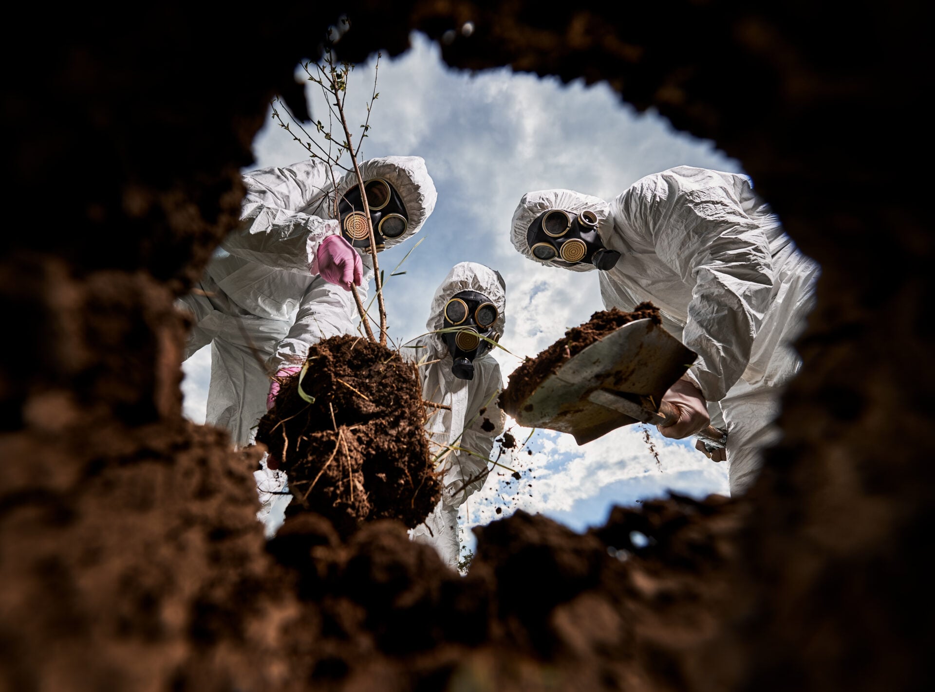 Ecologists digging pit by shovel and planting tree in polluted area.