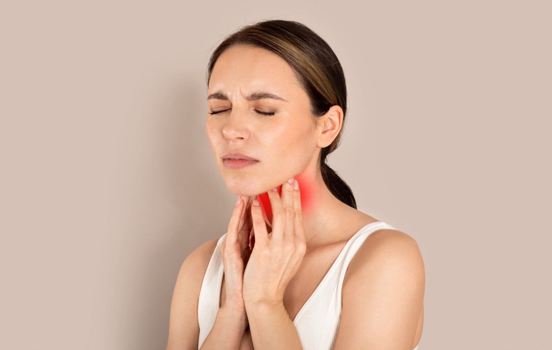 Woman suffering from sore throat, touching her neck, beige background